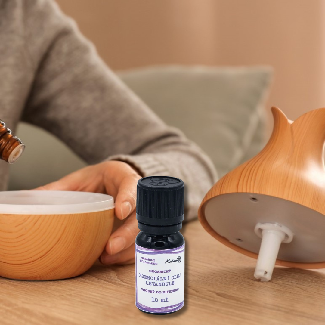 Lavender essential oil bottle on a wooden table between two aroma diffusers, with a person’s hand opening one of the diffusers in the background.